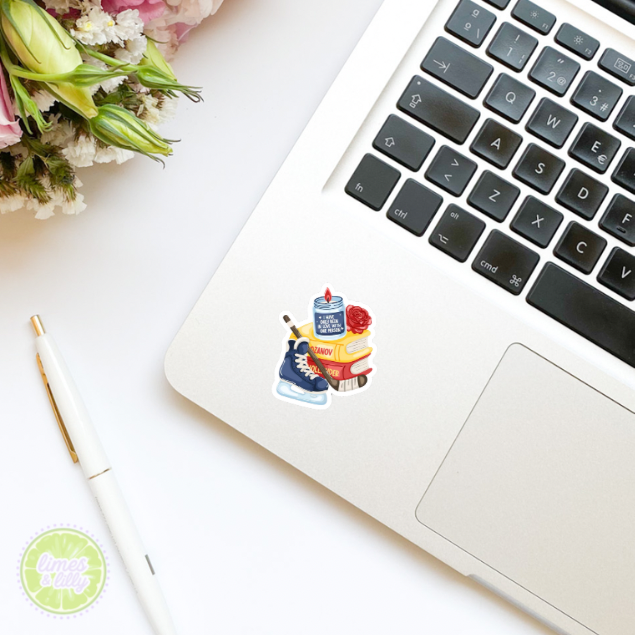 Laptop with a sticker on the palm rest area, next to a pen and flowers on a white surface.