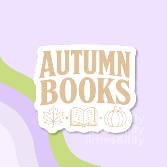A die-cut sticker with the words 'AUTUMN BOOKS' in large tan letters on a white background, decorated with simple tan line drawings of a maple leaf, an open book, and a pumpkin. The sticker is centered on a light lavender background with abstract green and lavender curved shapes.