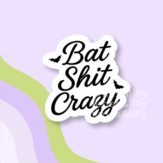 A die-cut vinyl sticker with the phrase 'Bat Shit Crazy' in black cursive script on a white background, accented with small black bat silhouettes. The sticker is displayed on a pastel purple background with abstract wavy stripes in light green and lavender.