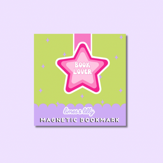 A square magnetic bookmark card with a pastel design, featuring a pink star outlined in white with the words 'BOOK LOVER' in the center, a pink ribbon graphic, and a lavender bottom border with the text 'limes & lily MAGNETIC BOOKMARK'. The product is centered on a light lavender background.