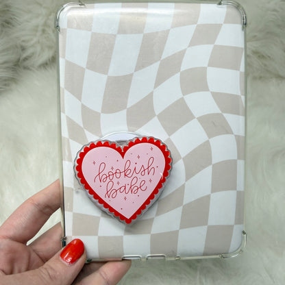 Checkered phone case with a heart-shaped 'bookish babe' badge held by a hand.