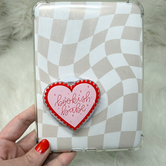Checkered phone case with a heart-shaped 'bookish babe' badge held by a hand.