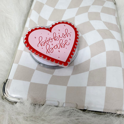 Heart-shaped pink and red object with 'bookish babe' text on a checkered surface