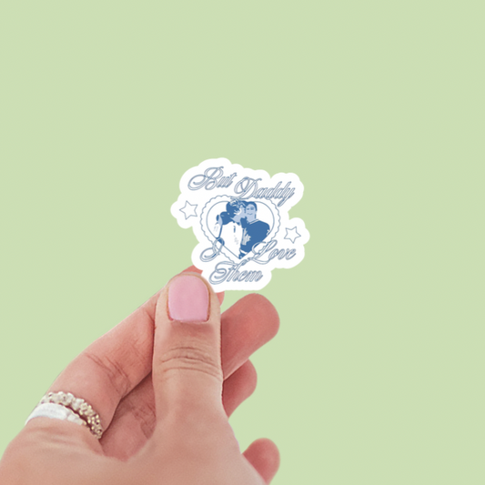 Hand holding a sticker with 'Girl Daddy Love Story' design on a light green background