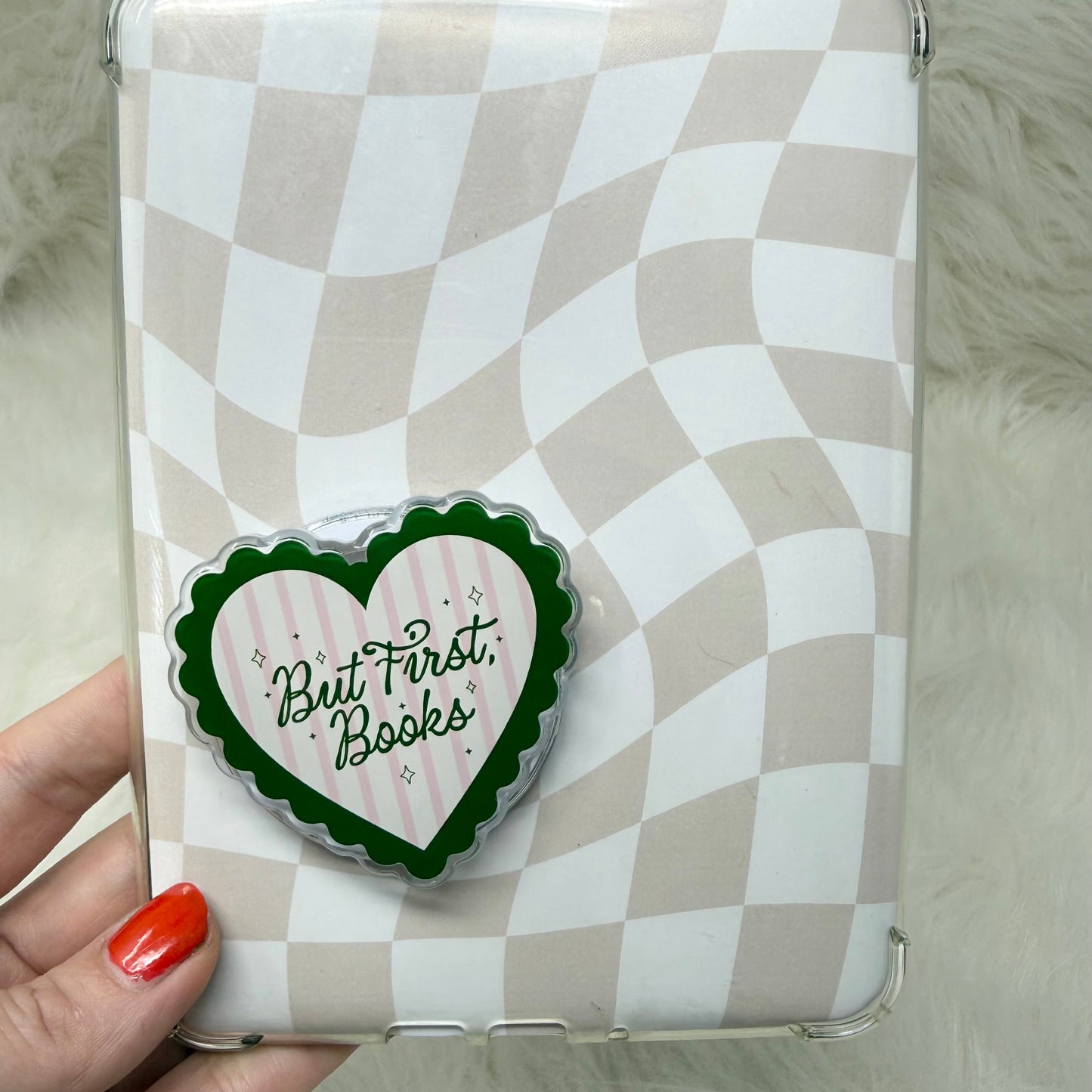 Checkered kindle case with a heart-shaped sticker reading 'But First, Books' held by a hand.