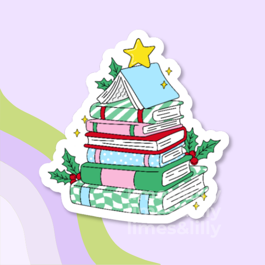 A die-cut sticker featuring an illustration of a Christmas book tree, with stacked books in pastel colors, holly leaves, red berries, and a yellow star on top, shown against a light lavender background with abstract green and purple shapes.