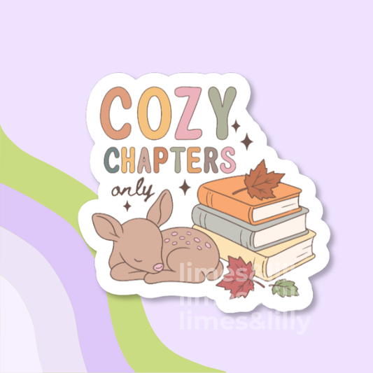 A die-cut sticker featuring the phrase 'COZY CHAPTERS only' in pastel lettering, with a sleeping deer and a stack of books decorated with autumn leaves, shown on a lavender background with abstract green and purple curved shapes.