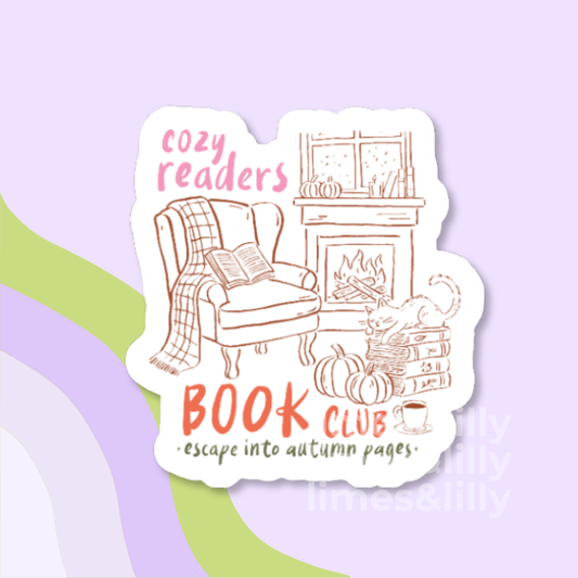 A die-cut sticker featuring an autumn-themed cozy reading scene with a chair, fireplace, books, pumpkins, and the text 'cozy readers BOOK CLUB escape into autumn pages.' The sticker is shown on a pastel lavender background with abstract green and lavender curved shapes.