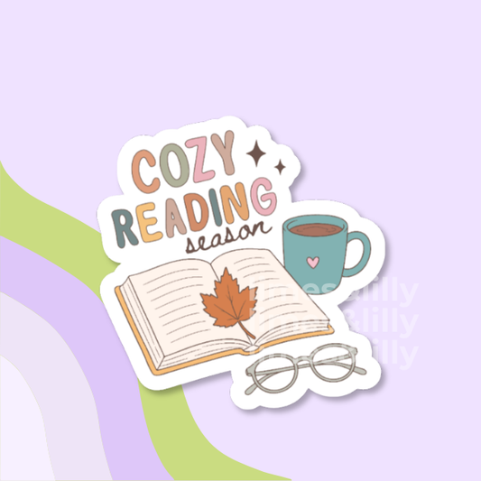 A die-cut sticker with a white border featuring Halloween-themed illustrations and the text 'read MORE books' in black and orange, shown on a pastel purple background with abstract green and lavender shapes.