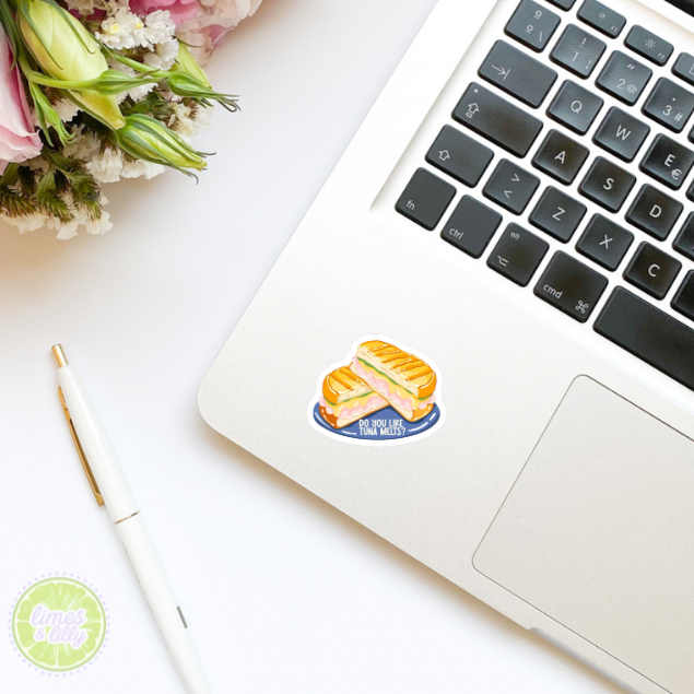 Laptop with a sticker of a cake on a white surface with flowers and a pen.