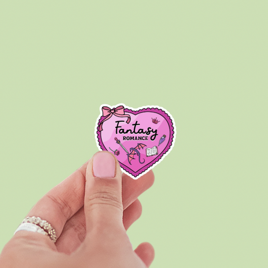 Heart-shaped sticker with 'Fantasy Romance' text held by a hand on a light green background