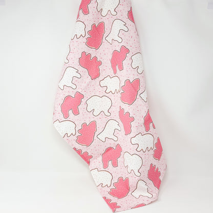 Pink cotton tea towel featuring pink and white frosted animal cookies with colorful sprinkles