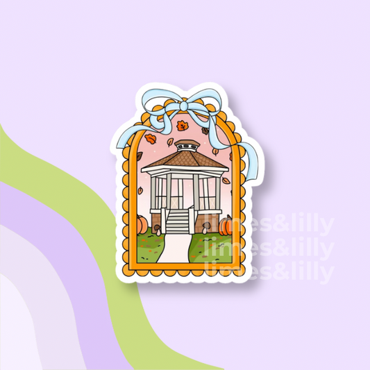A die-cut sticker featuring a whimsical illustration of a gazebo surrounded by pumpkins and autumn leaves, framed by a scalloped orange border with a light blue bow at the top. The sticker is shown on a pastel lavender background with abstract wavy stripes in green and purple.