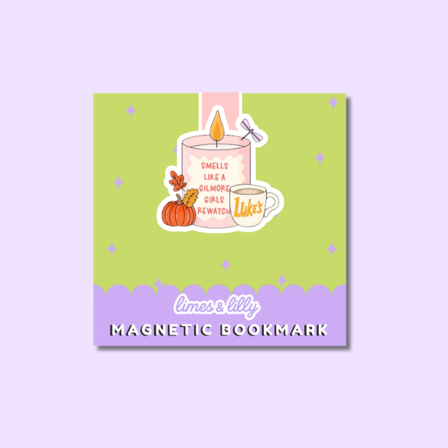 A square magnetic bookmark with a pastel design, featuring a light green center, a lavender bottom band, and an illustration of a pink candle, pumpkin, mug, and a dragonfly. The text reads 'limes & lilly' and 'MAGNETIC BOOKMARK'.