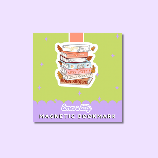 A square product card for a magnetic bookmark featuring an illustrated stack of books with autumn leaves and the title 'A Sweet Love Story.' The card has a light green upper section, a lavender lower section, and the text 'limes & lily' and 'MAGNETIC BOOKMARK.
