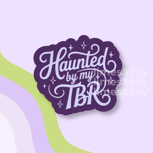 A die-cut sticker with the phrase 'Haunted by my TBR' in white script and block lettering on a dark purple background, shown on a pastel lavender background with abstract curved stripes in green, lavender, and white. A faint 'times&lilly' watermark is visible across the center-right.