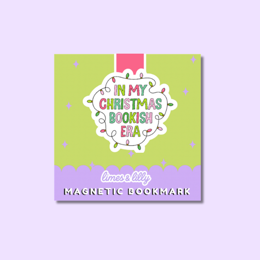 A square magnetic bookmark card with a pastel green and lavender design, featuring the text 'IN MY CHRISTMAS BOOKISH ERA' in colorful lettering inside a cloud outline with Christmas lights, and 'limes & lily MAGNETIC BOOKMARK' at the bottom. The card is centered on a light lavender background.