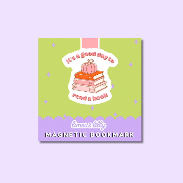 A square magnetic bookmark with a pastel design, featuring a lime green top section, a lavender bottom band, and a central illustration of stacked books with a small pumpkin and the phrase 'it's a good day to read a book'. The text 'limes & lily' and 'MAGNETIC BOOKMARK' are visible on the product, which is centered on a light lavender background.