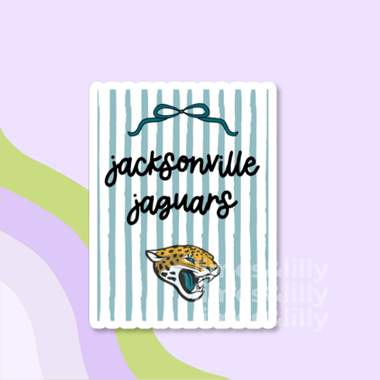 A rectangular sticker with a white background and vertical light blue stripes, featuring the text 'jacksonville jaguars' in black script, a dark blue bow illustration, and the Jacksonville Jaguars logo. The sticker is shown on a pastel purple background with abstract green and lavender shapes.