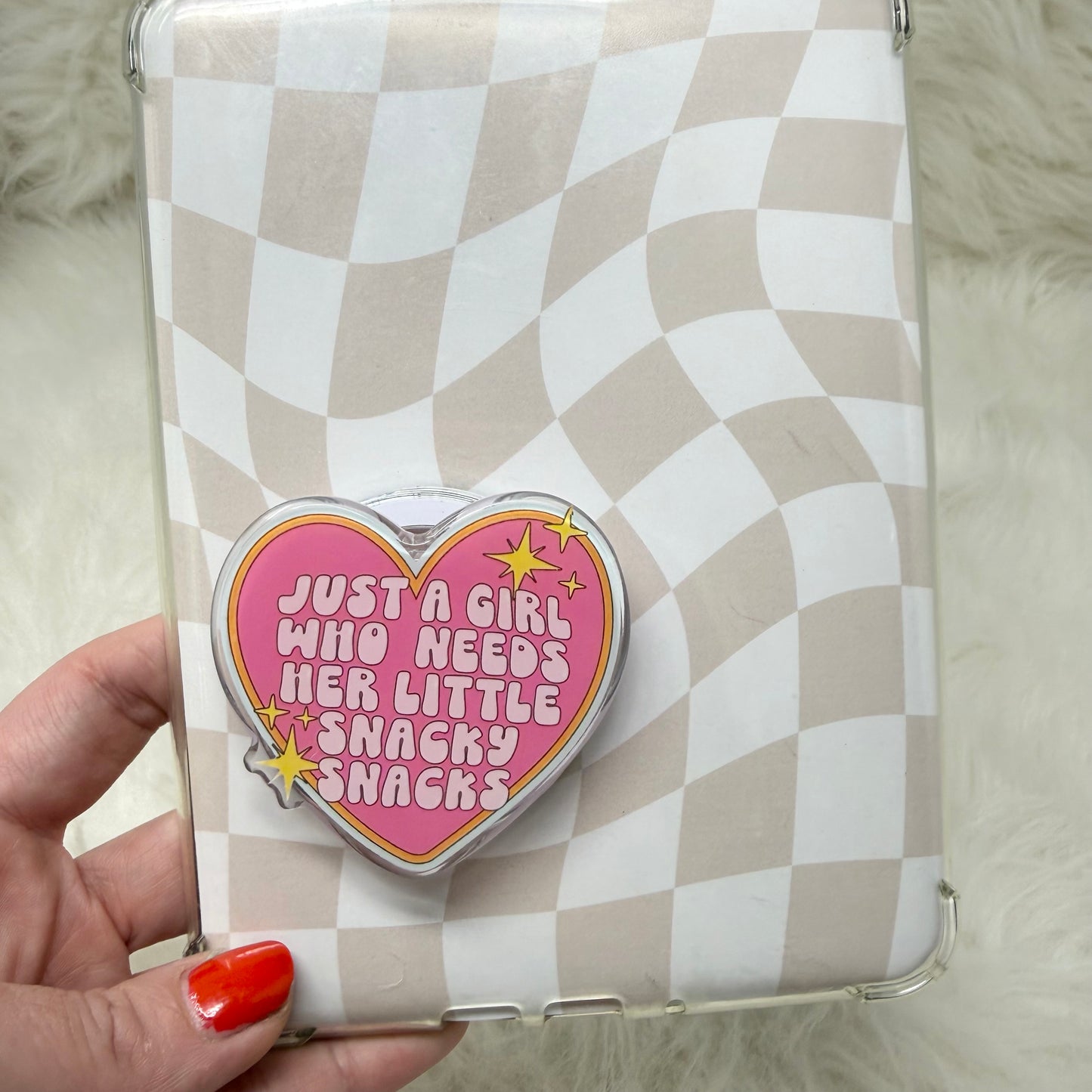 Phone case with a heart-shaped design and text, held by a hand with red nail polish.