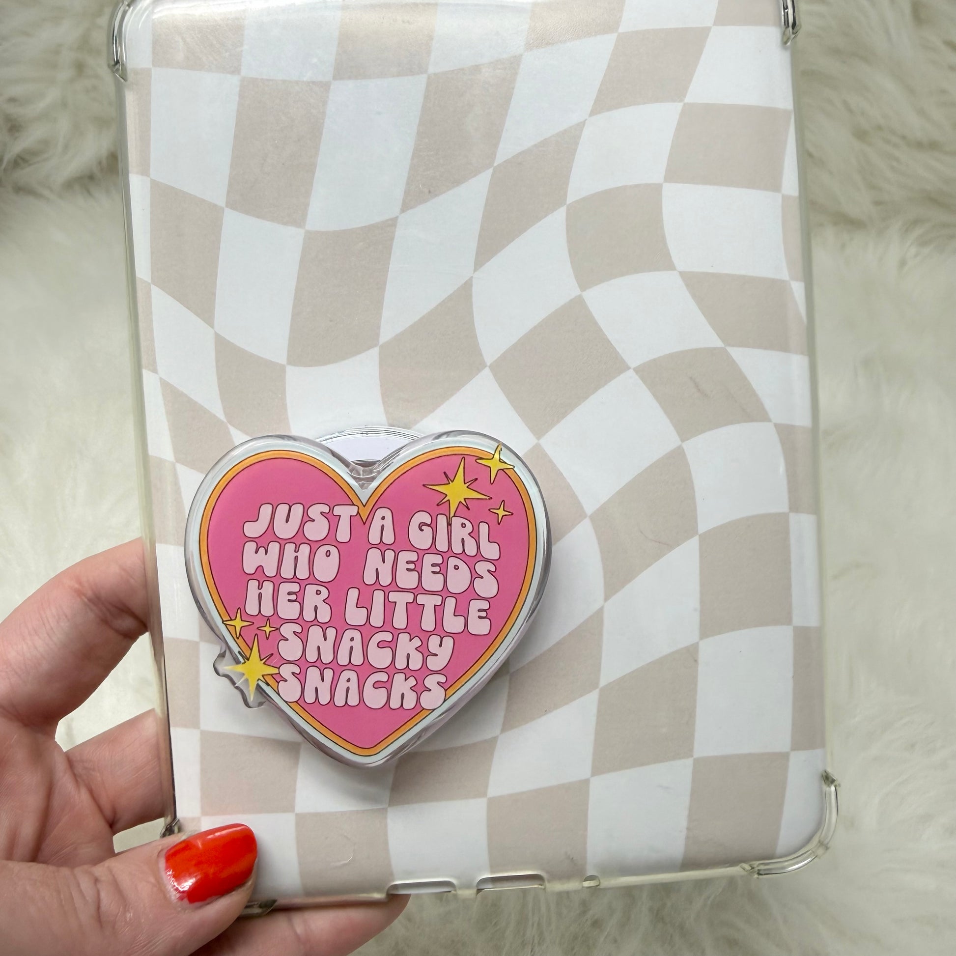 Phone case with a heart-shaped design and text, held by a hand with red nail polish.