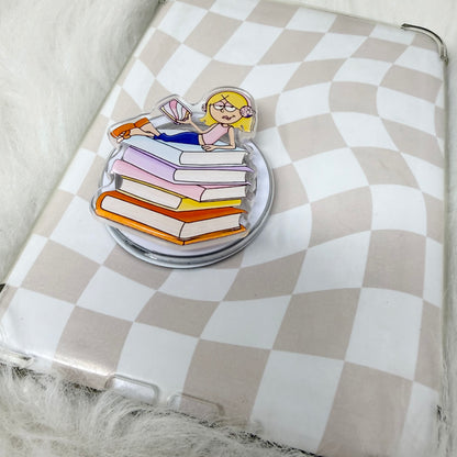 Pin with a design of a person reading a book on a stack of books, placed on a checkered surface.