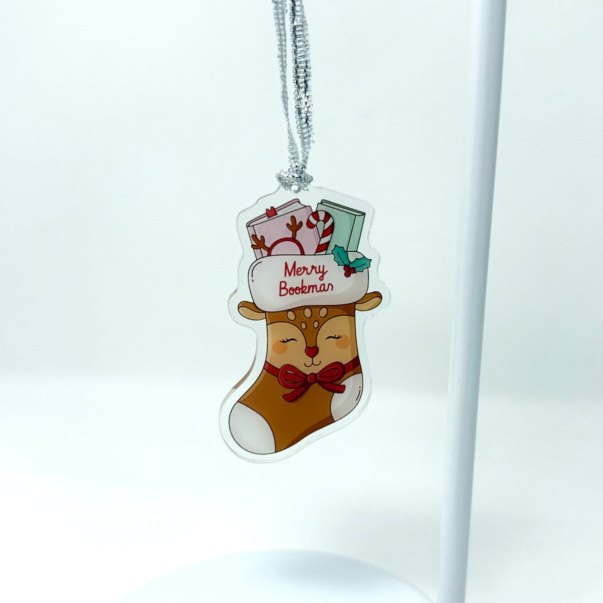 A Christmas stocking ornament featuring a cartoon reindeer wearing a red bow tie and a white hat that reads 'Merry Boobman' with holiday gifts, hanging from a silver string against a white background.