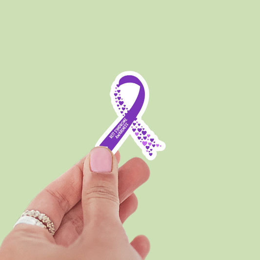 Hand holding a purple ribbon with 'Rett syndrome Awareness' text on a light green background