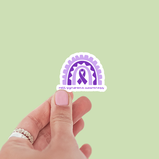 Hand holding a sticker with a purple ribbon design on a light green background
