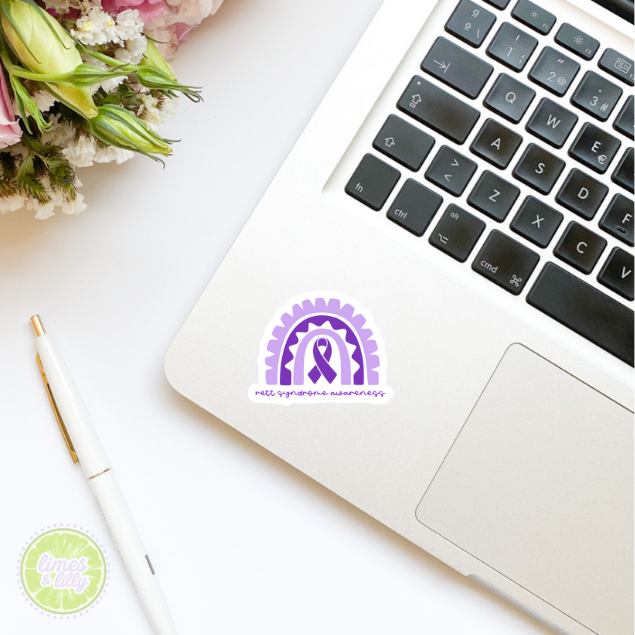 Laptop with a purple ribbon sticker on a white surface with flowers and a pen.