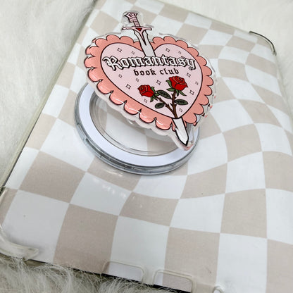 Phone ring holder with 'Romantic Book Club' design on a checkered surface