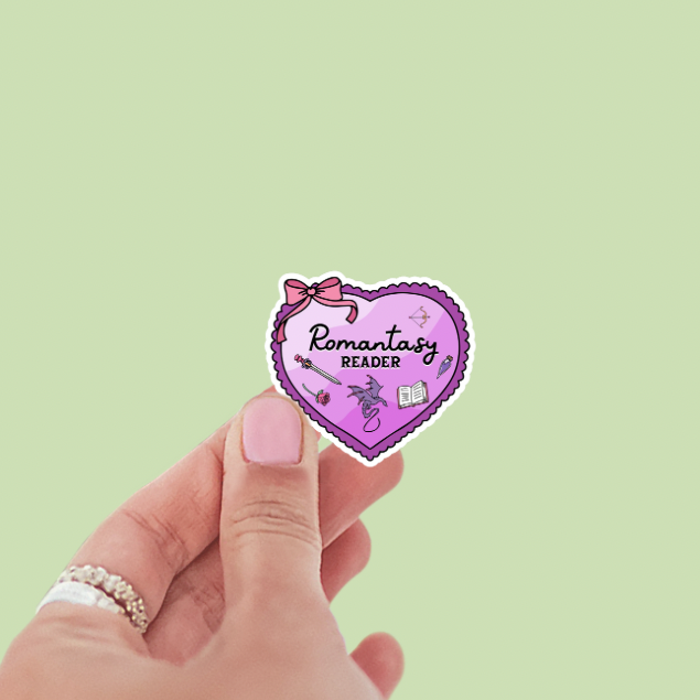Heart-shaped sticker with 'Romantasy Reader' text held by a hand on a light green background