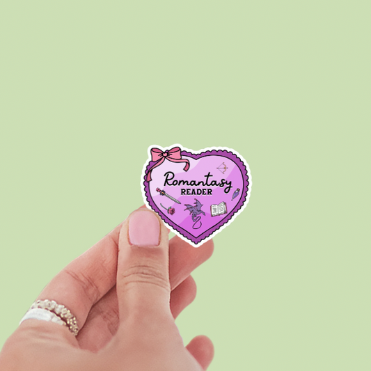 Heart-shaped sticker with 'Romantasy Reader' text held by a hand on a light green background