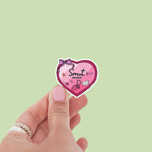 Heart-shaped sticker with 'Smut' text held by a hand on a light green background