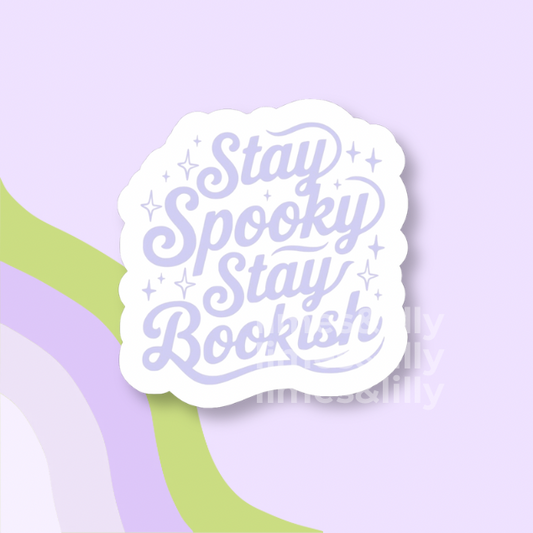 A die-cut sticker with the phrase 'Stay Spooky Stay Bookish' in lavender script on a white background, shown on a pastel purple backdrop with abstract green and lavender curved shapes.