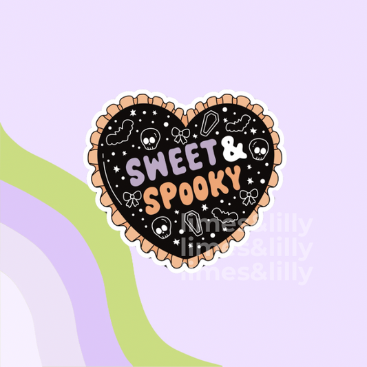 A heart-shaped sticker with a scalloped peach border, featuring a black background decorated with white skulls, candy corn, bats, and stars, with the words 'SWEET & SPOOKY' in pastel purple, pink, and orange lettering. The sticker is shown on a light purple background with abstract wavy stripes in green and lavender.