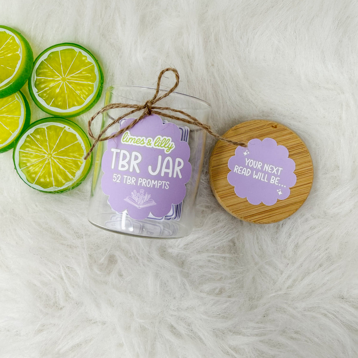 Top view of a glass TBR reading-prompt jar with bamboo lid, twine bow, and lime slices